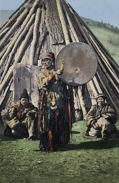 Altai shaman with a tambourine on the background of a traditional dwelling - chaadyr